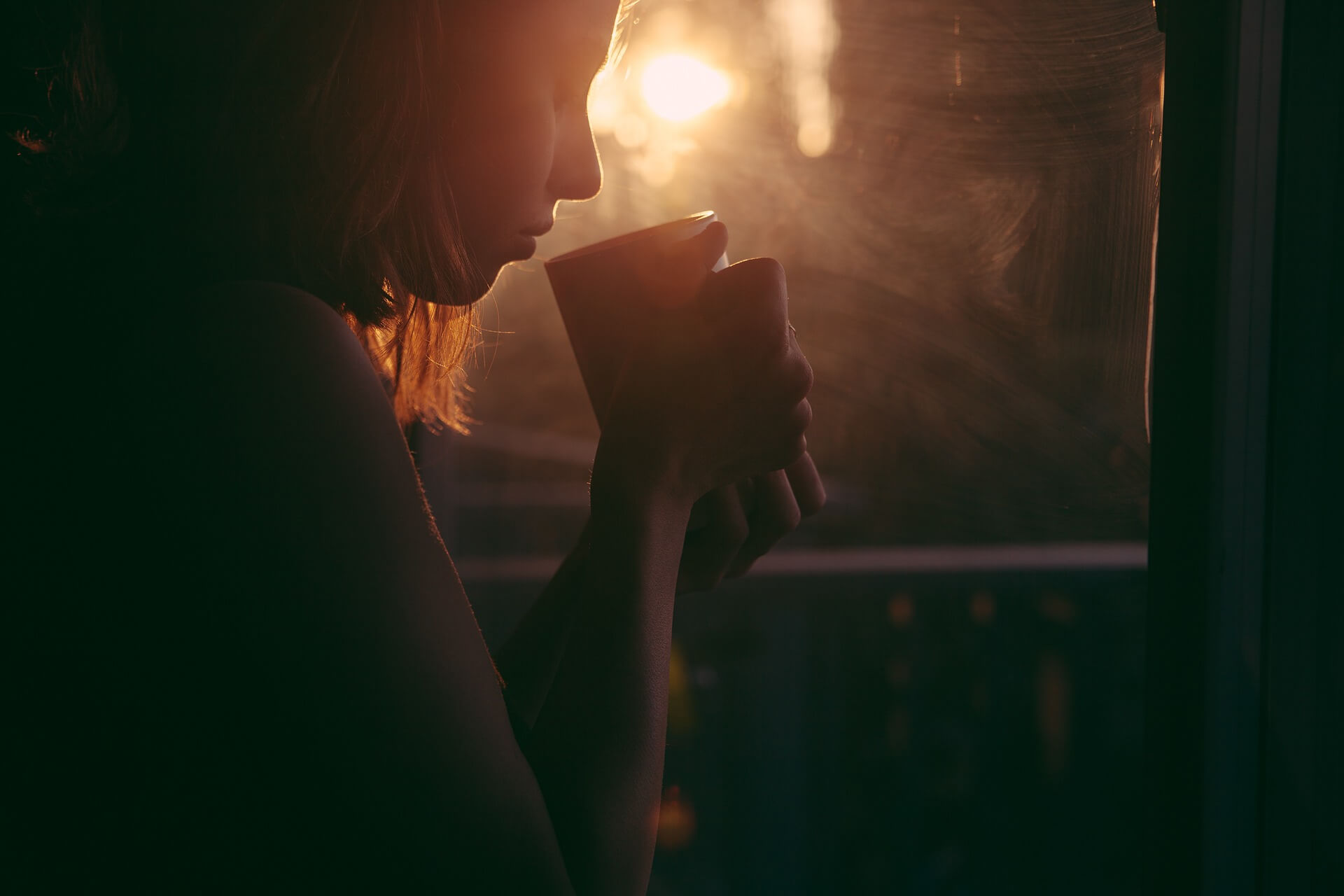 woman holding coffee near a window at sunset