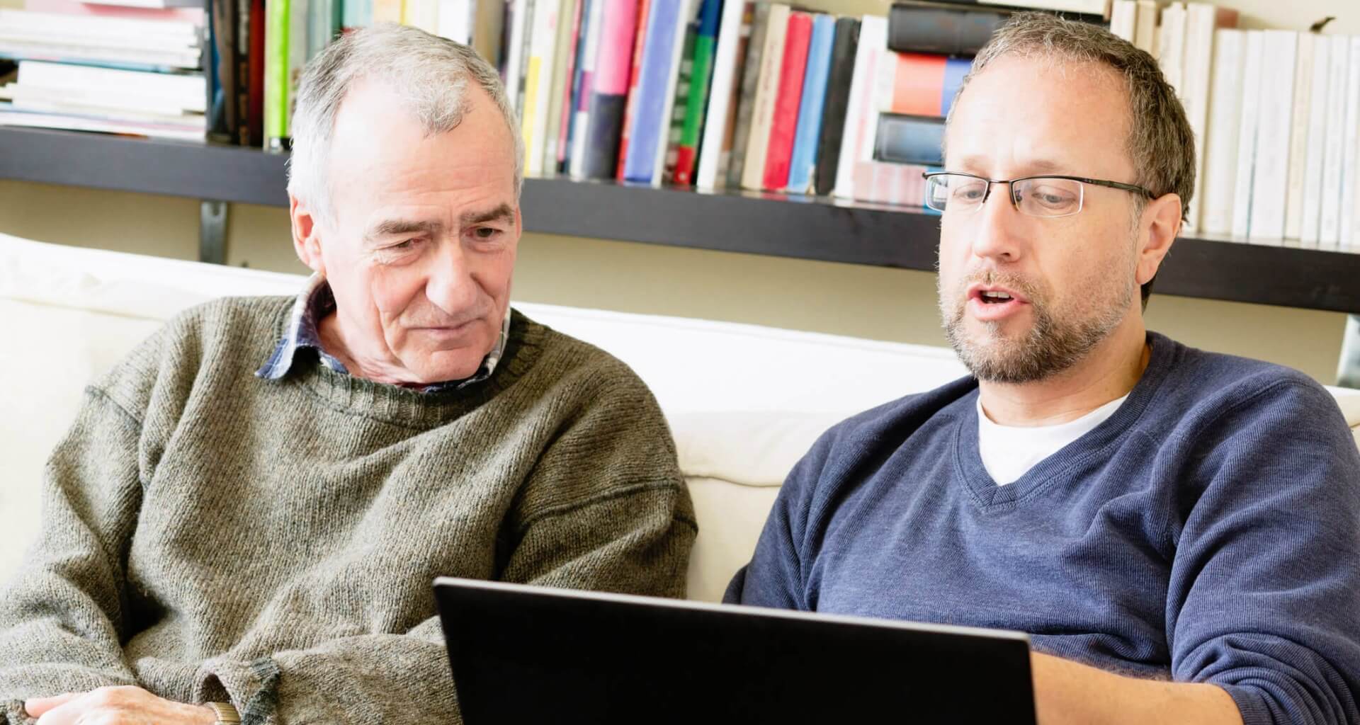 son showing older father how to use laptop