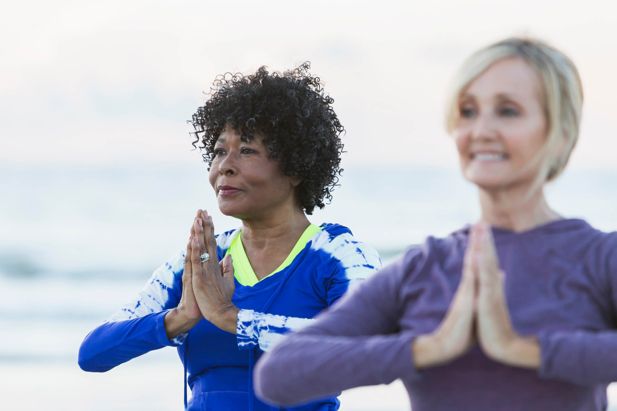 two older women holding their hands near their chest in yoga psoe